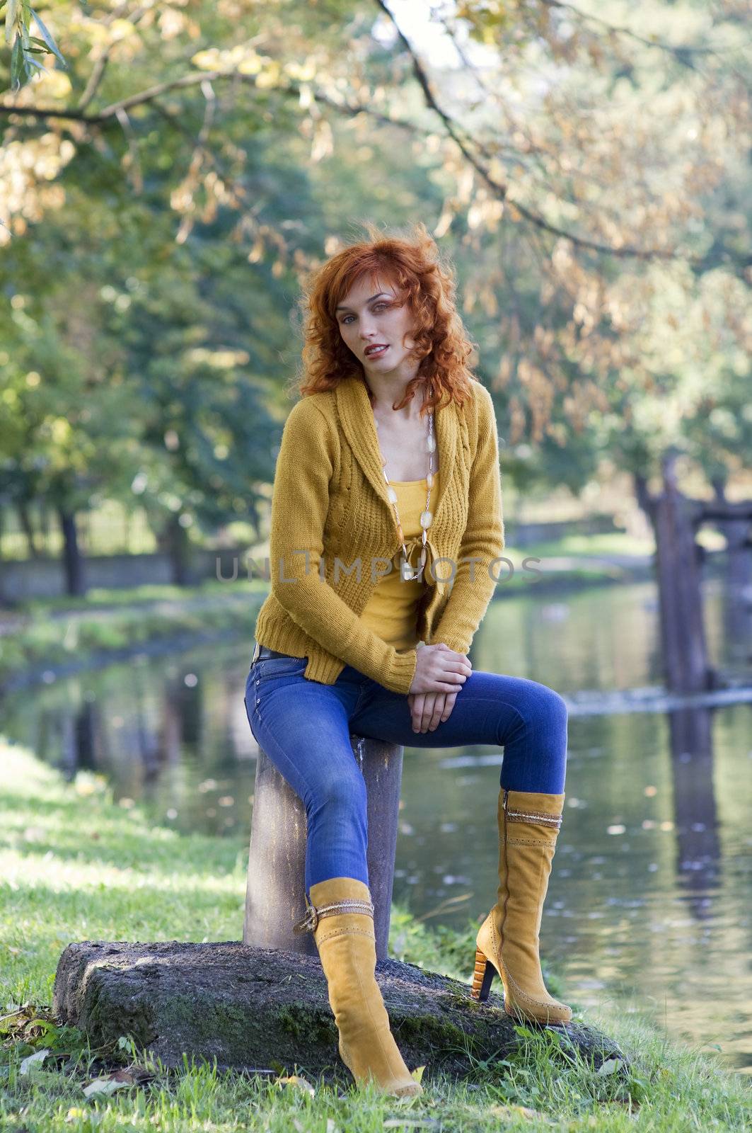 pretty woman red haired sitting near river in yellow autumn dress