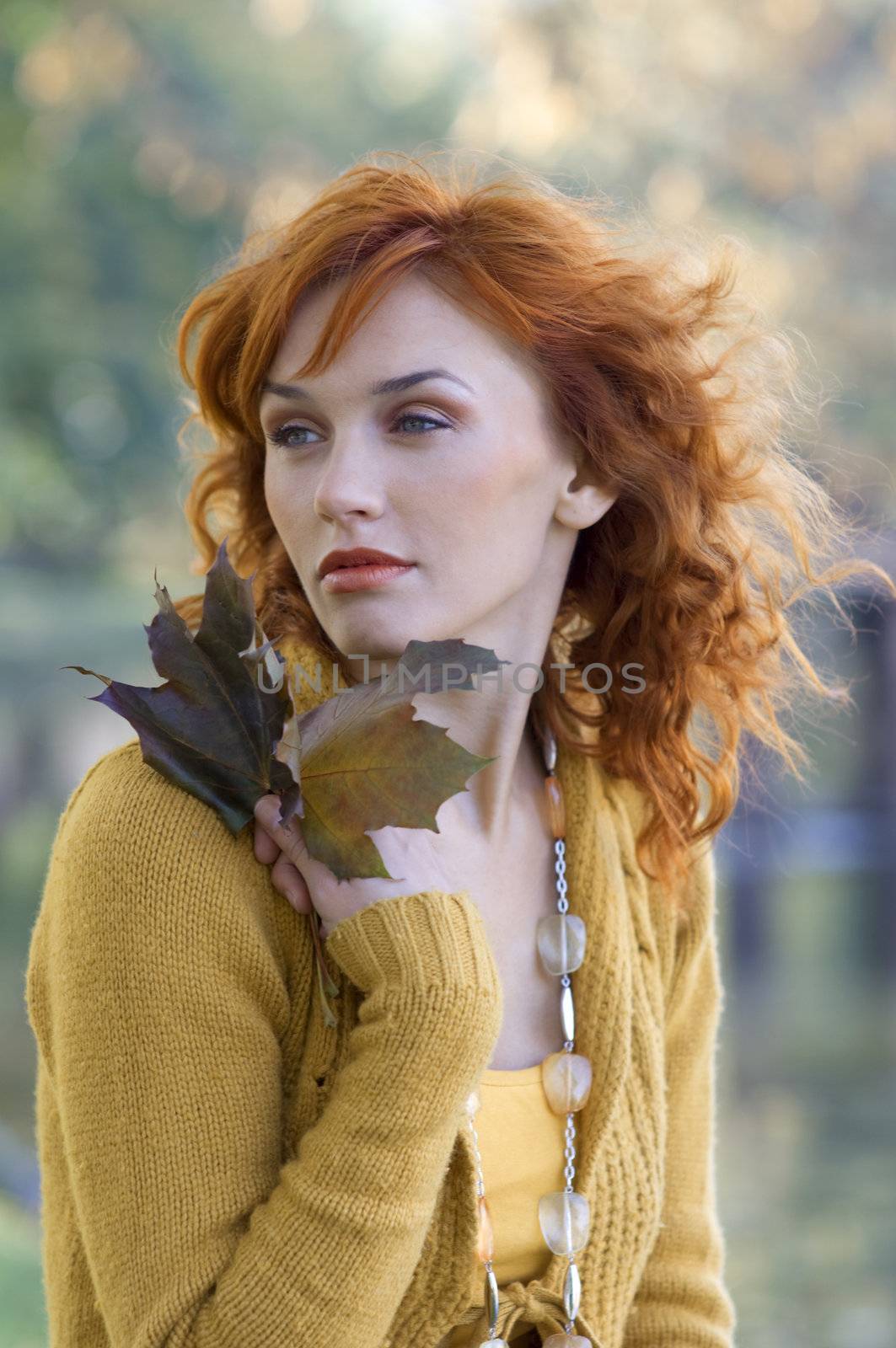 close up of red-haired woman with some leaves near face in park