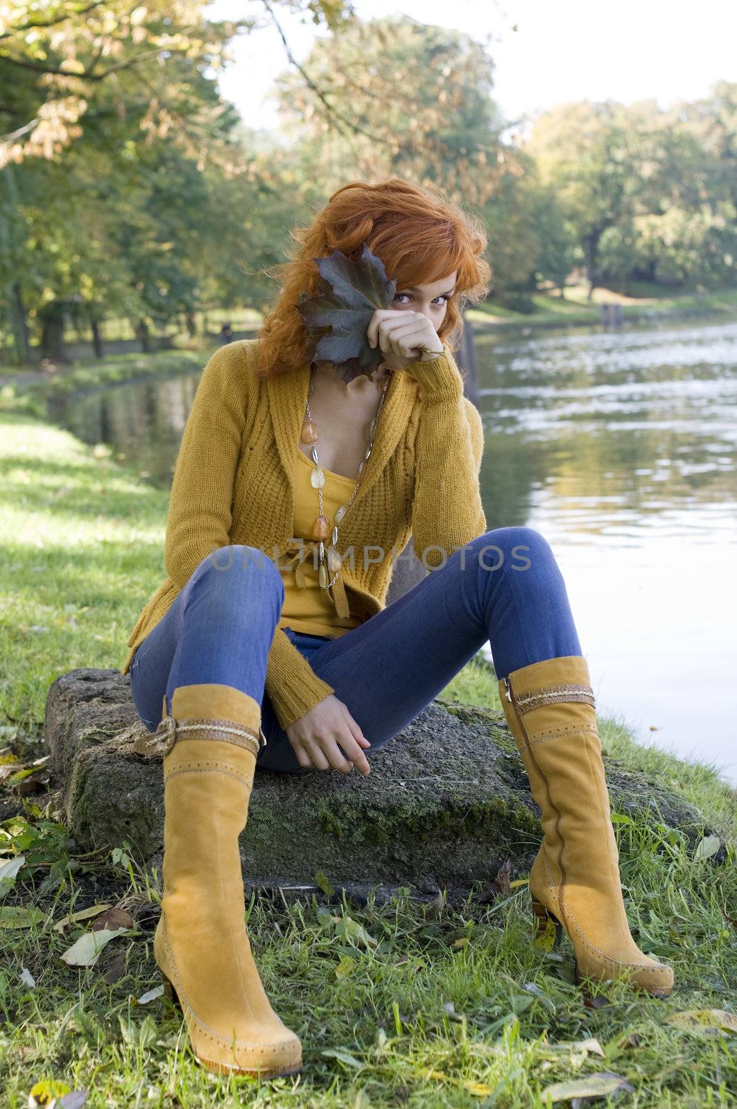 beautiful woman sitting near river playing with some leaves in autumn