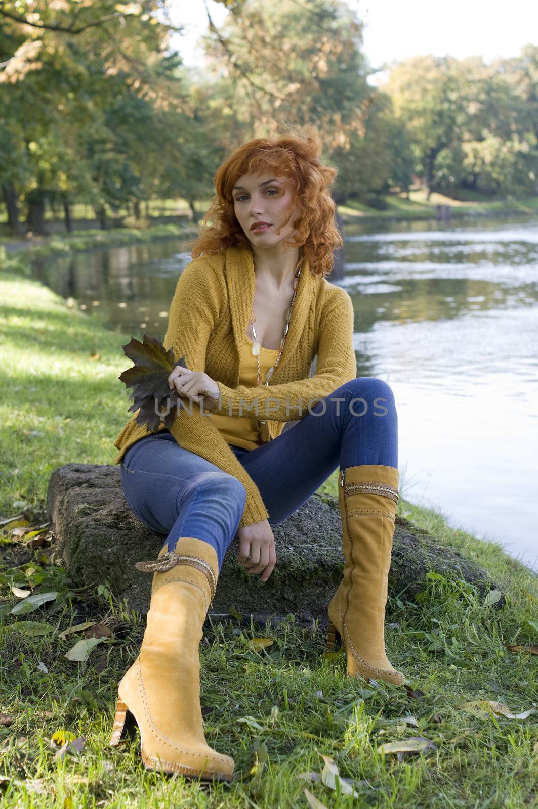 beautiful woman sitting near river in a park in autumn season