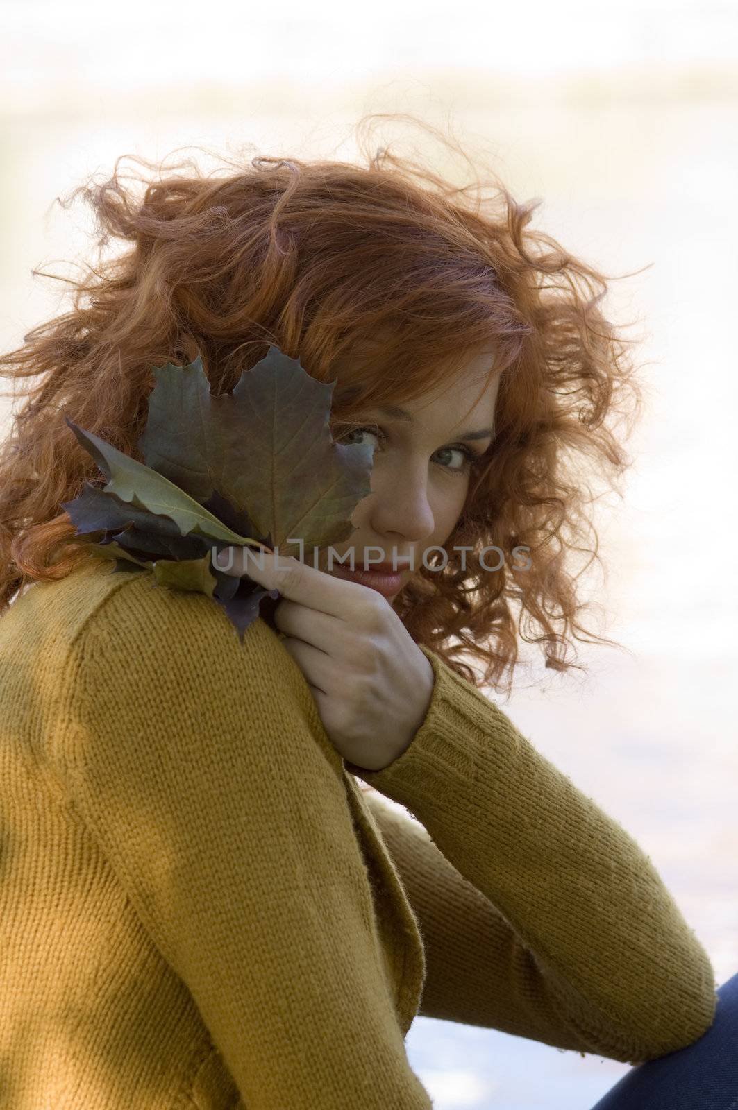 romantic portrait of a young woman with her face behind autumn leaves