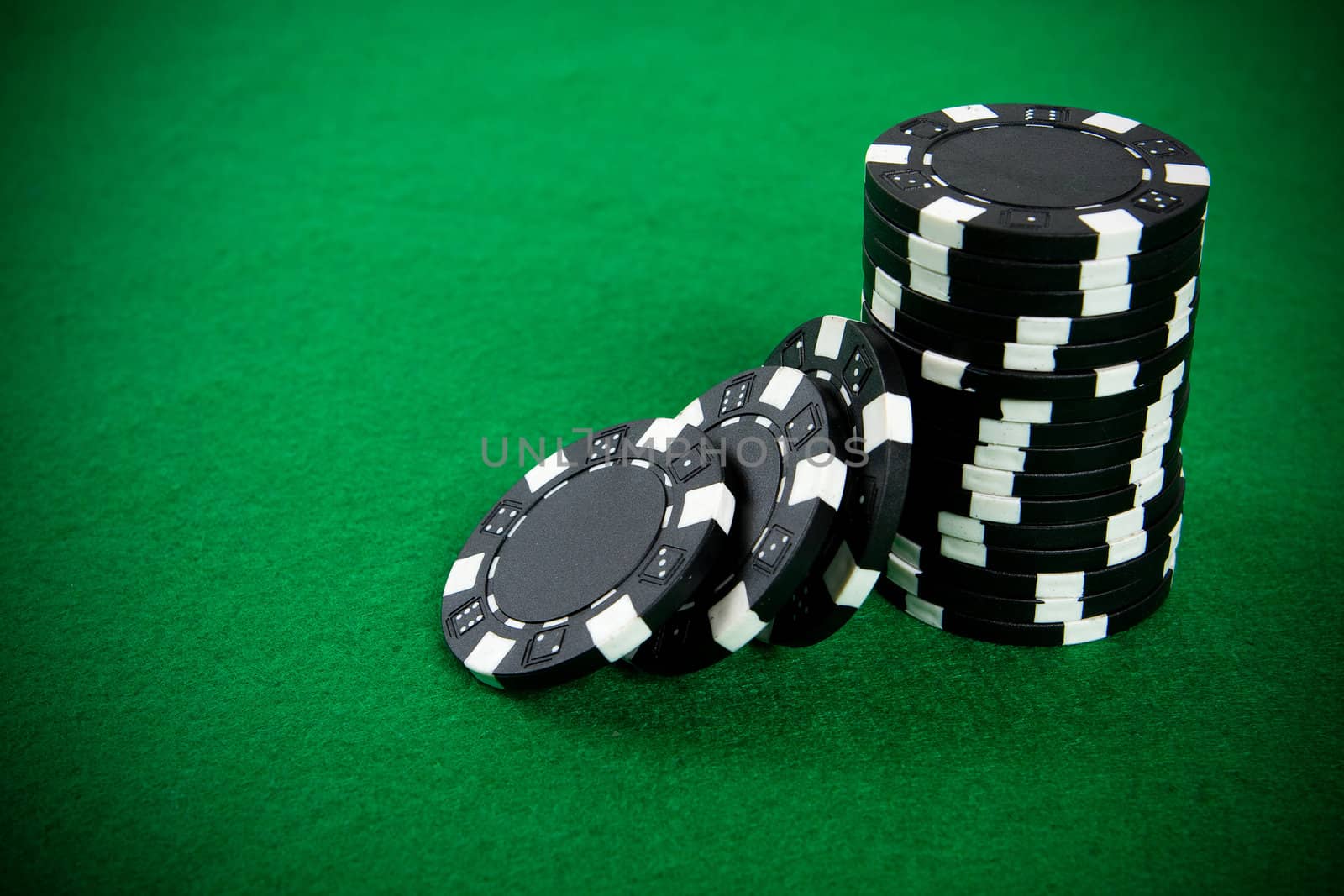 Stack of black poker chips on a green poker table background.