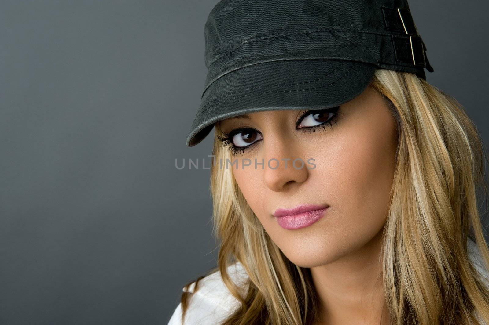a young, stylish and beautiful girl wearing a hat with blonde hair and pink lip stick on neutral gray background