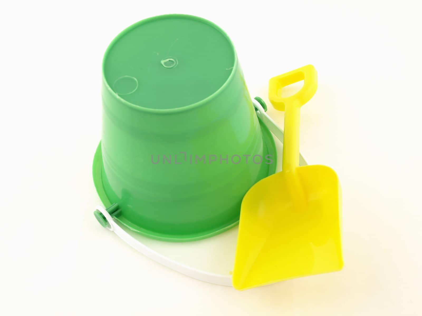 A green plastic bucket upside down with a shovel isolated on a white background