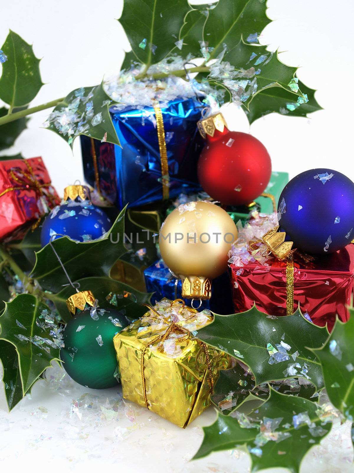 Colorful gift boxes, Christmas bulbs and holly, sprinkled with artificial snow. Isolated on a white background.