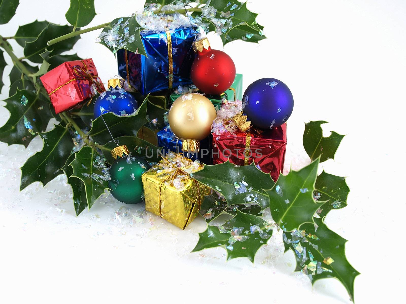 Colorful gift boxes, Christmas bulbs and holly, sprinkled with artificial snow. Isolated on a white background.
