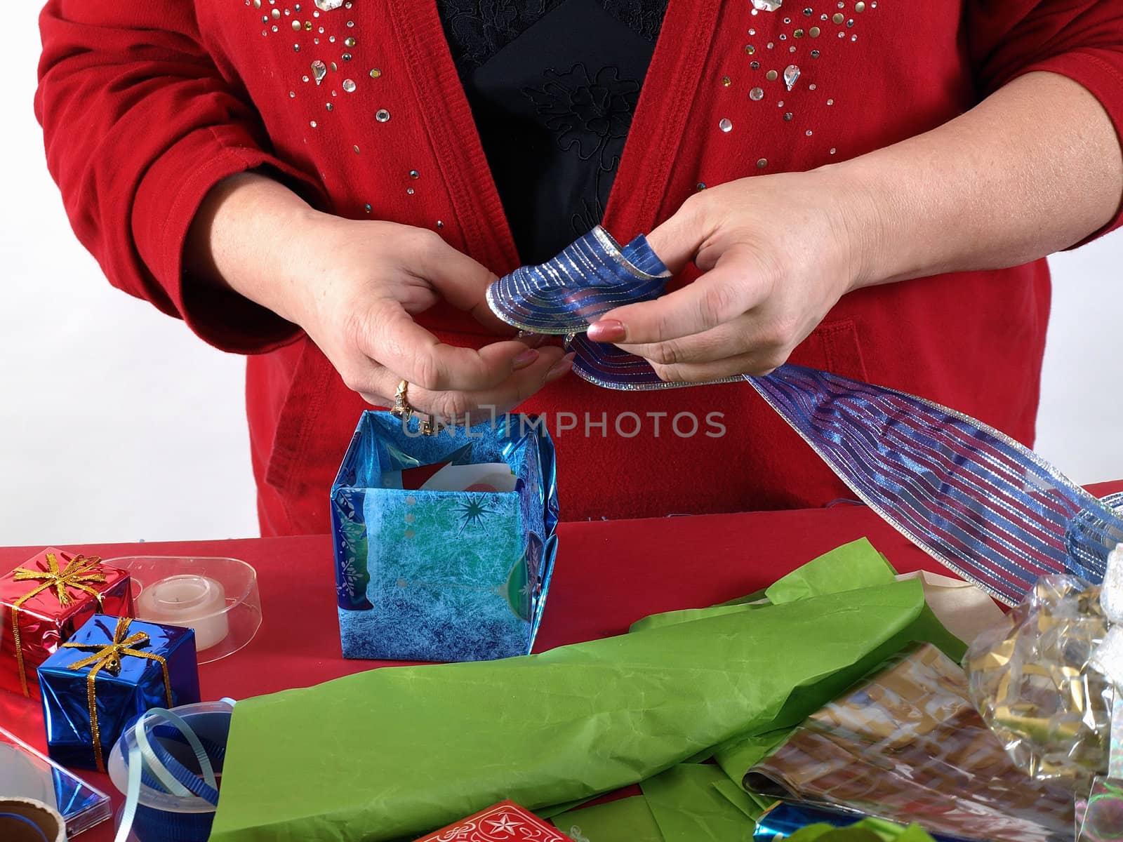 A woman forms a blue bow out of a shiny ribbon as she wraps a present.