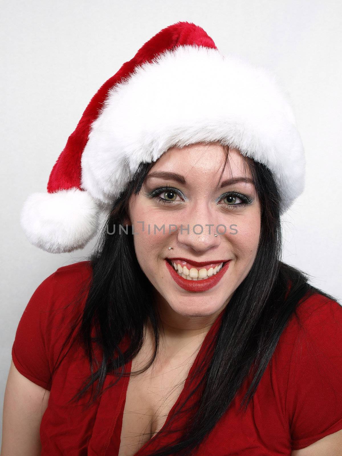 A pretty young pierced adult woman in a Santa hat cheerfully smiles.