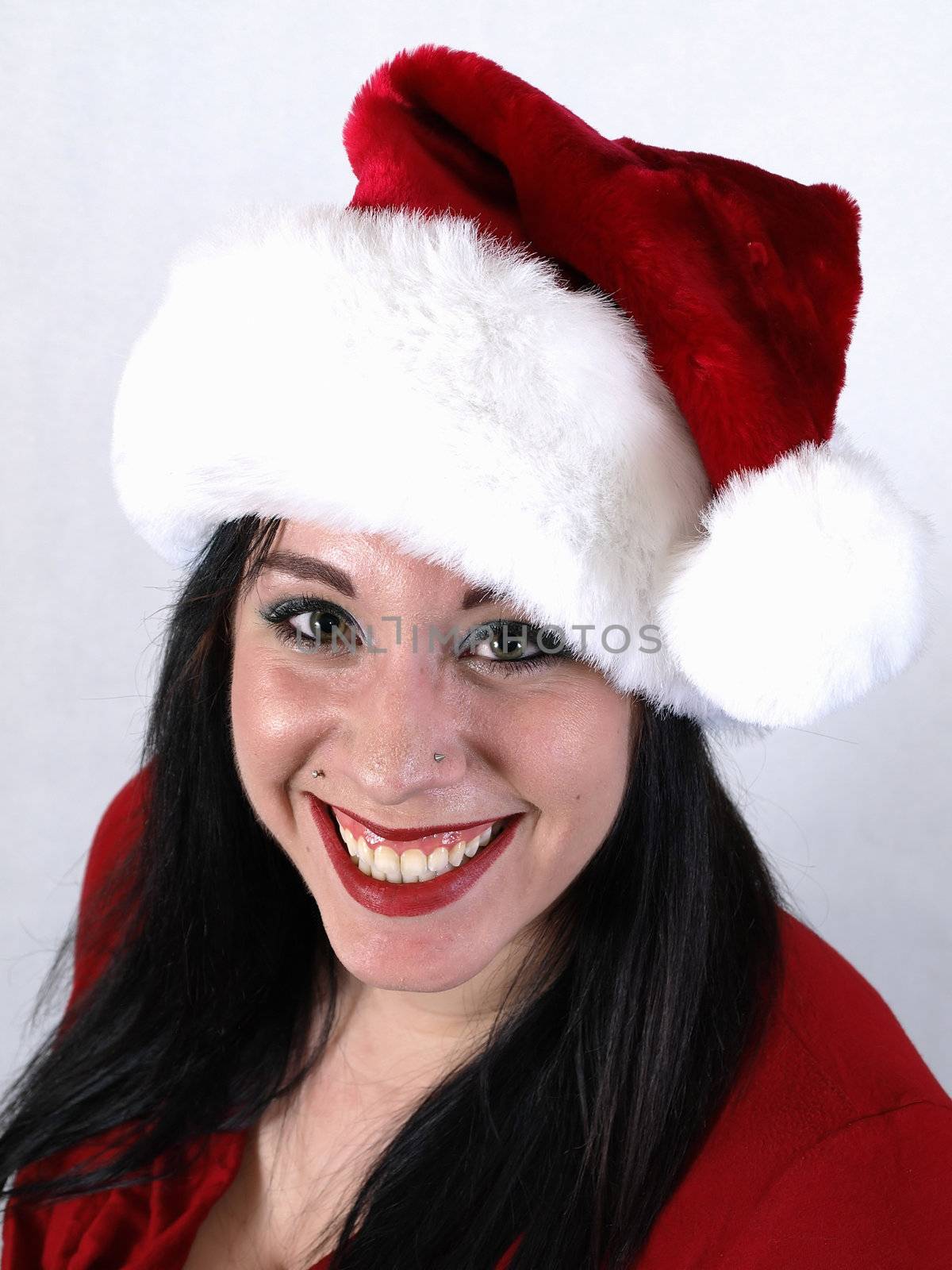 A pretty young pierced adult woman in a Santa hat cheerfully smiles.
