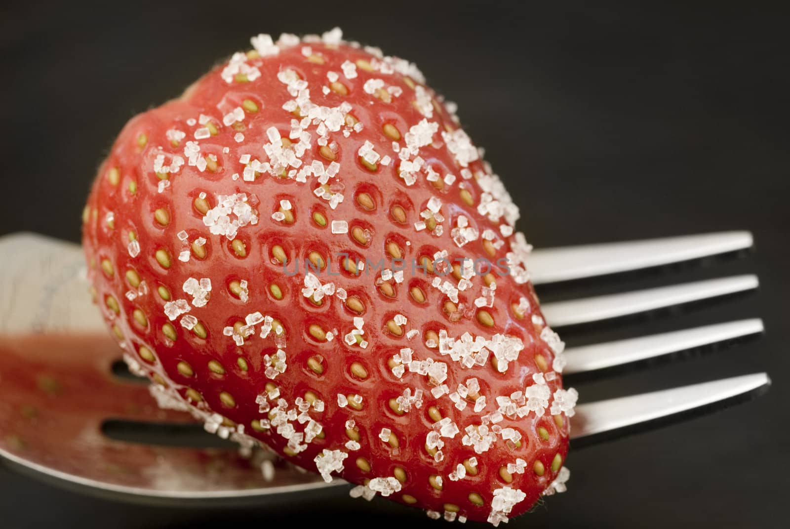 ripe red strawberry on a fork coated in sugar granuals