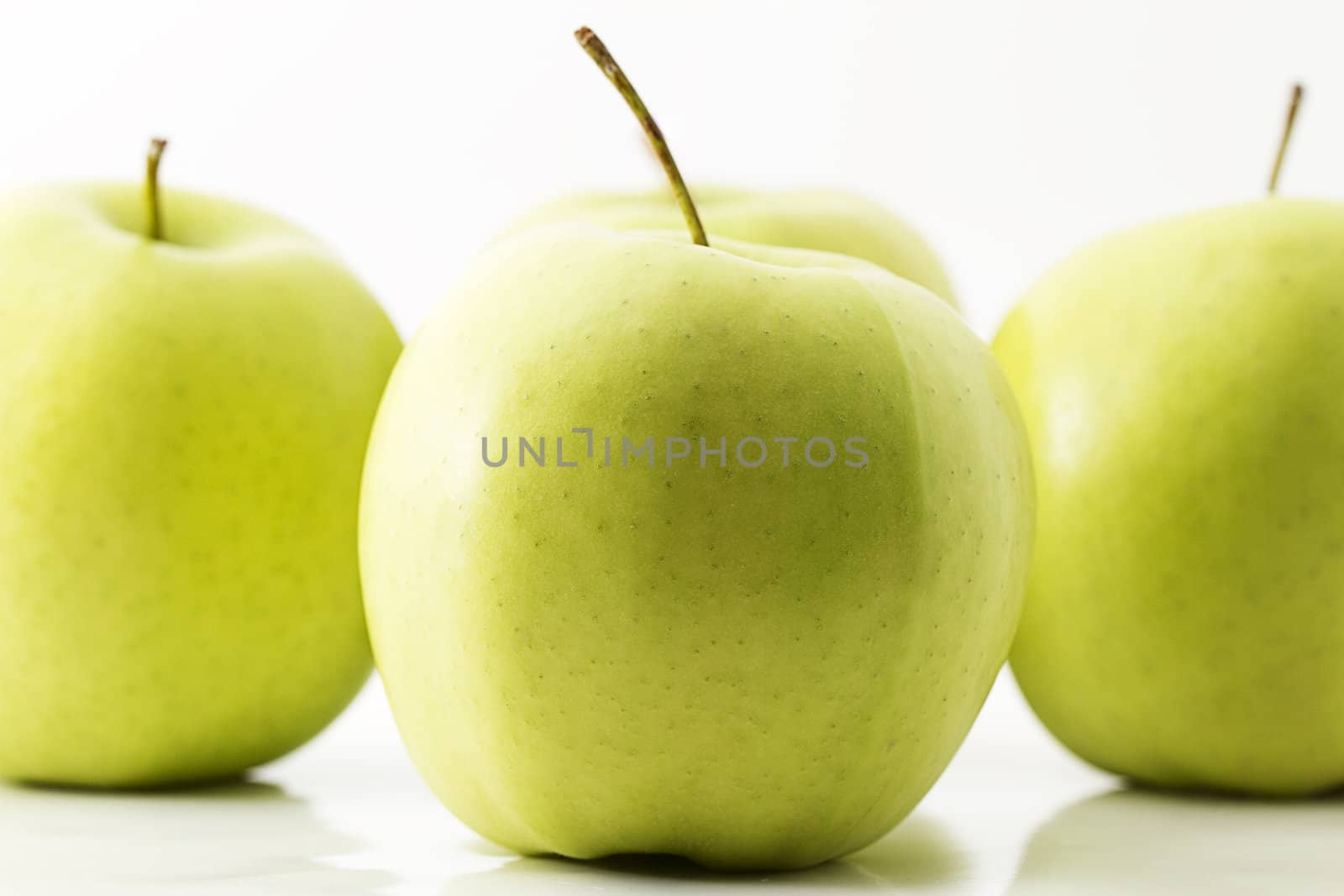 one green apple in front of three green apples on white background