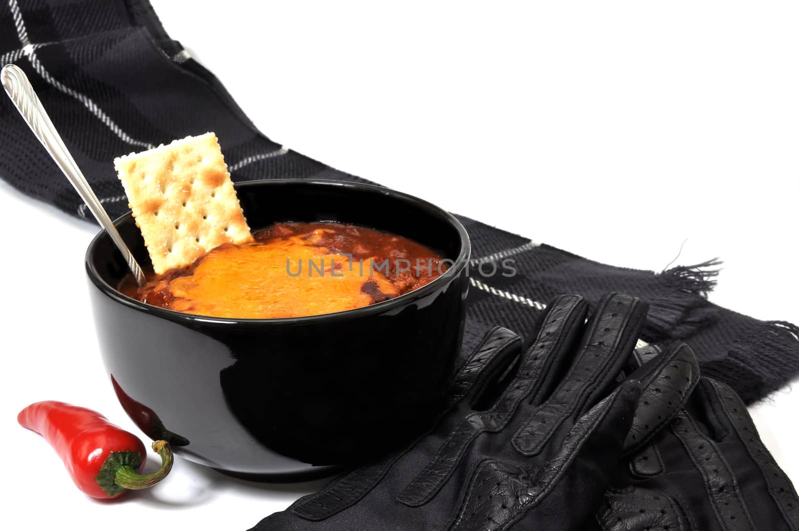 Bowl of chili with melted cheese, cracker, red cayenne pepper, spoon, scarf, and gloves.  Isolated on white background.