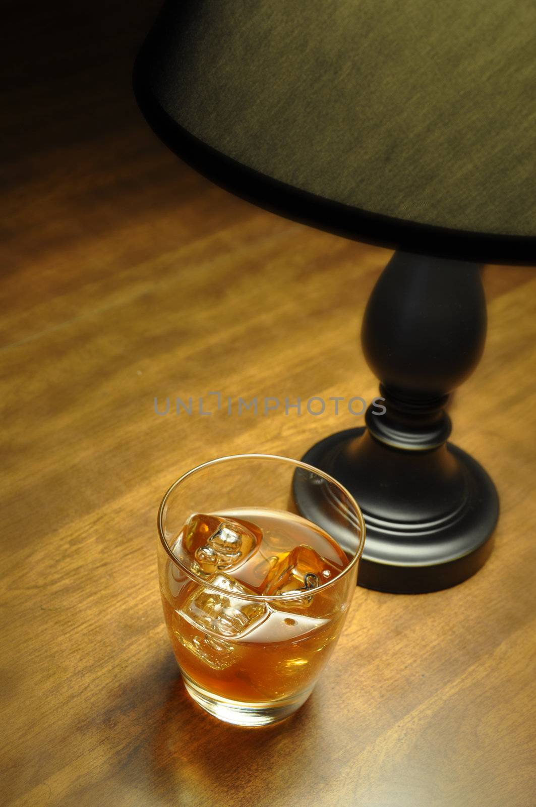 Bourbon on the rocks on wooden table illuminated by lamp.  