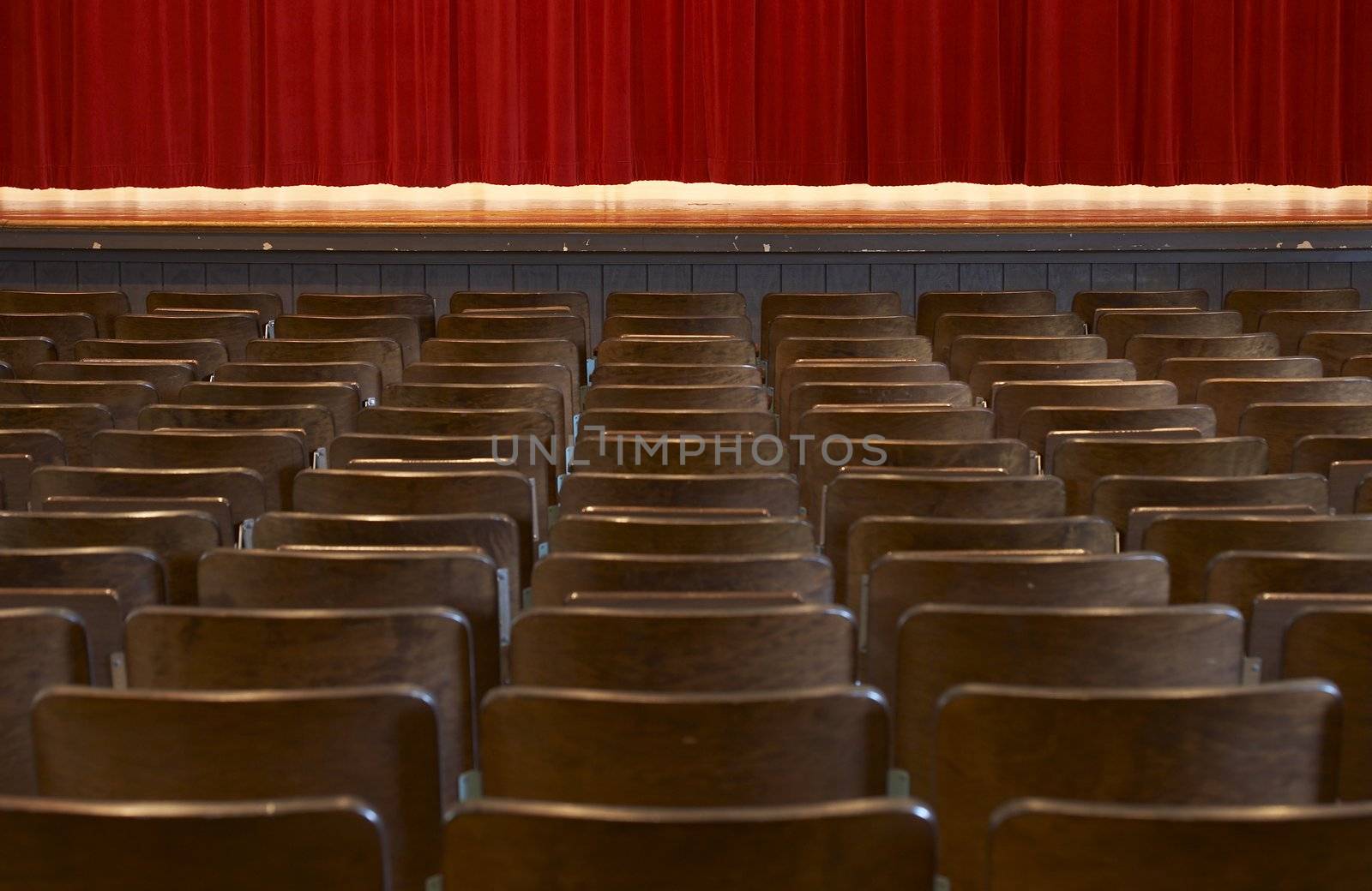 rows of wood chairs in an old auditorium and a red curtain