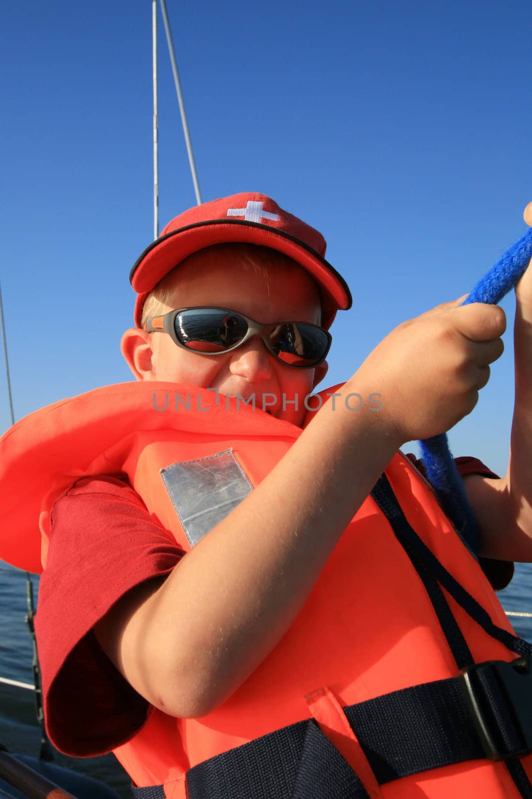 Boy in the life jacket with sunglasses on the yacht. He is pulling sheets (ropes). Work aboard, sailing.
