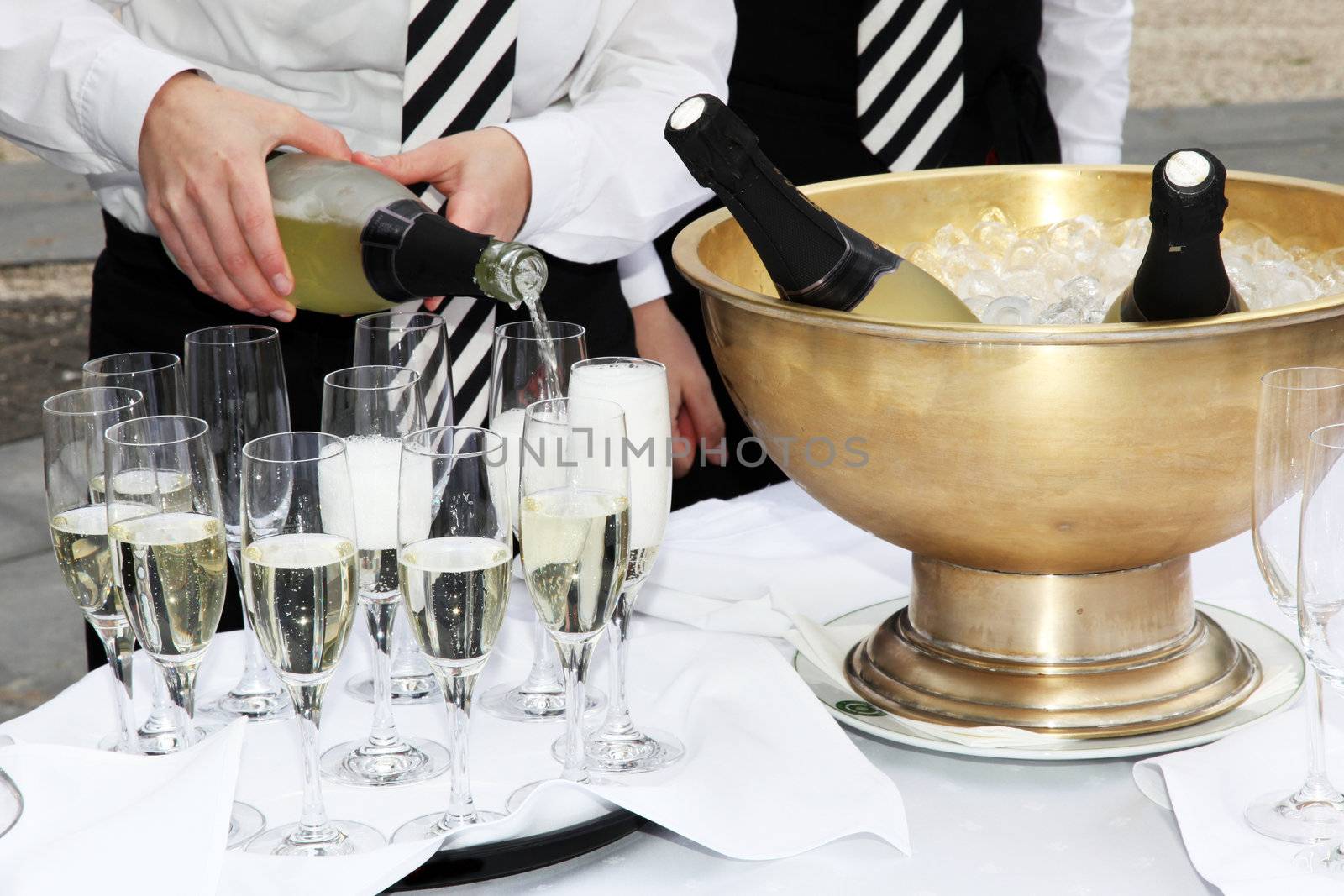 Two waiters fill glasses of champagne at a party.