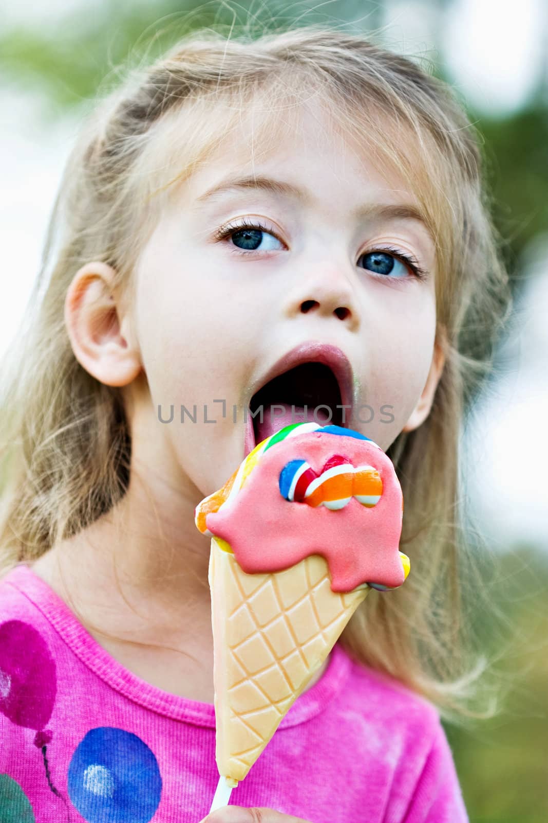 Little girl licking a sucker that is in the shape of an ice cream cone.