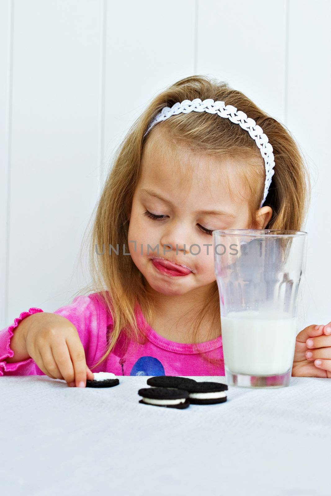 Little girl eating creme filled cookies while drinking a glass of milk. 