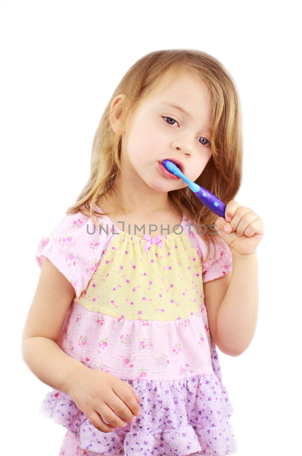 Cute little girl in pink pajamas is brushing her teeth against a white background.

