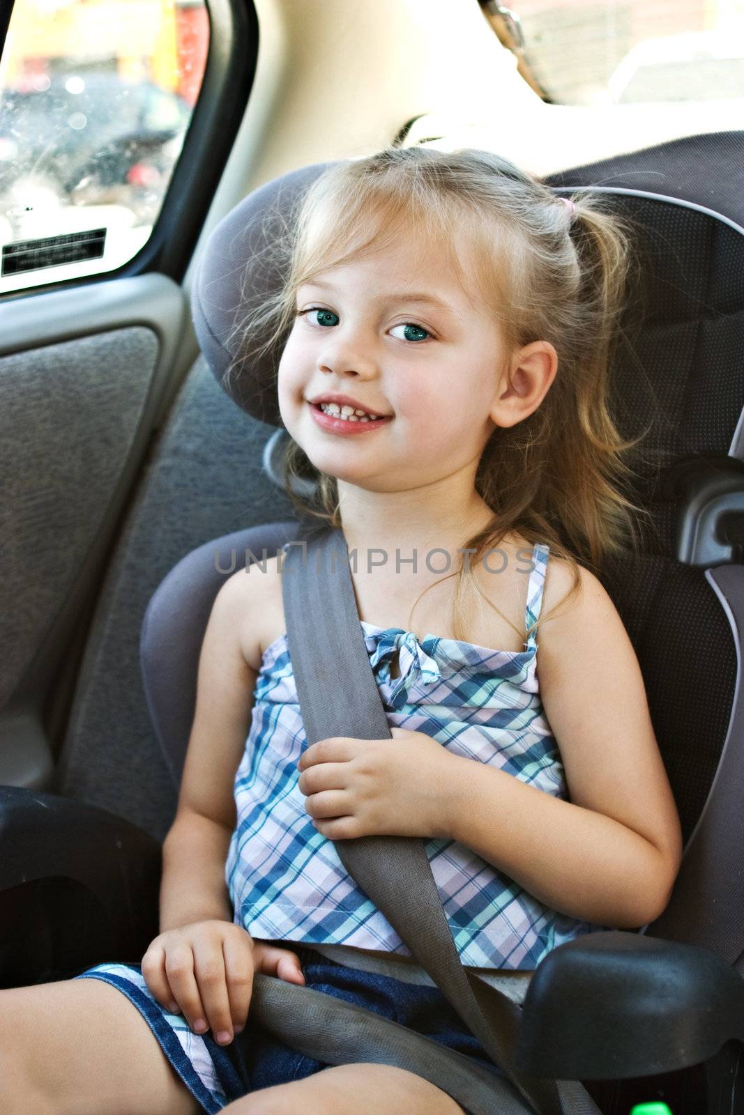 Little girl in a car seat smiles at viewer.