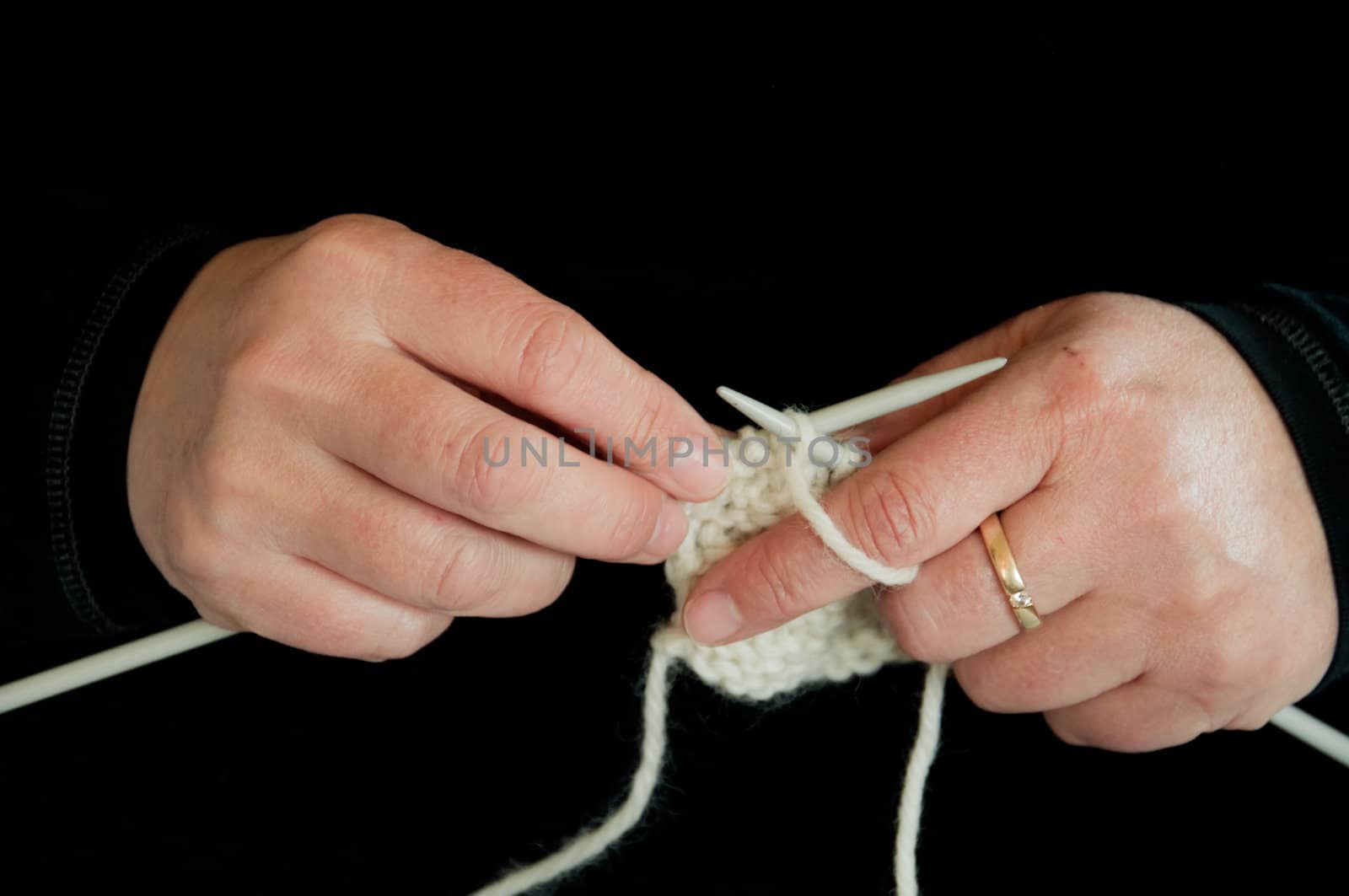 Close-up of a pair of knitting hands with black background