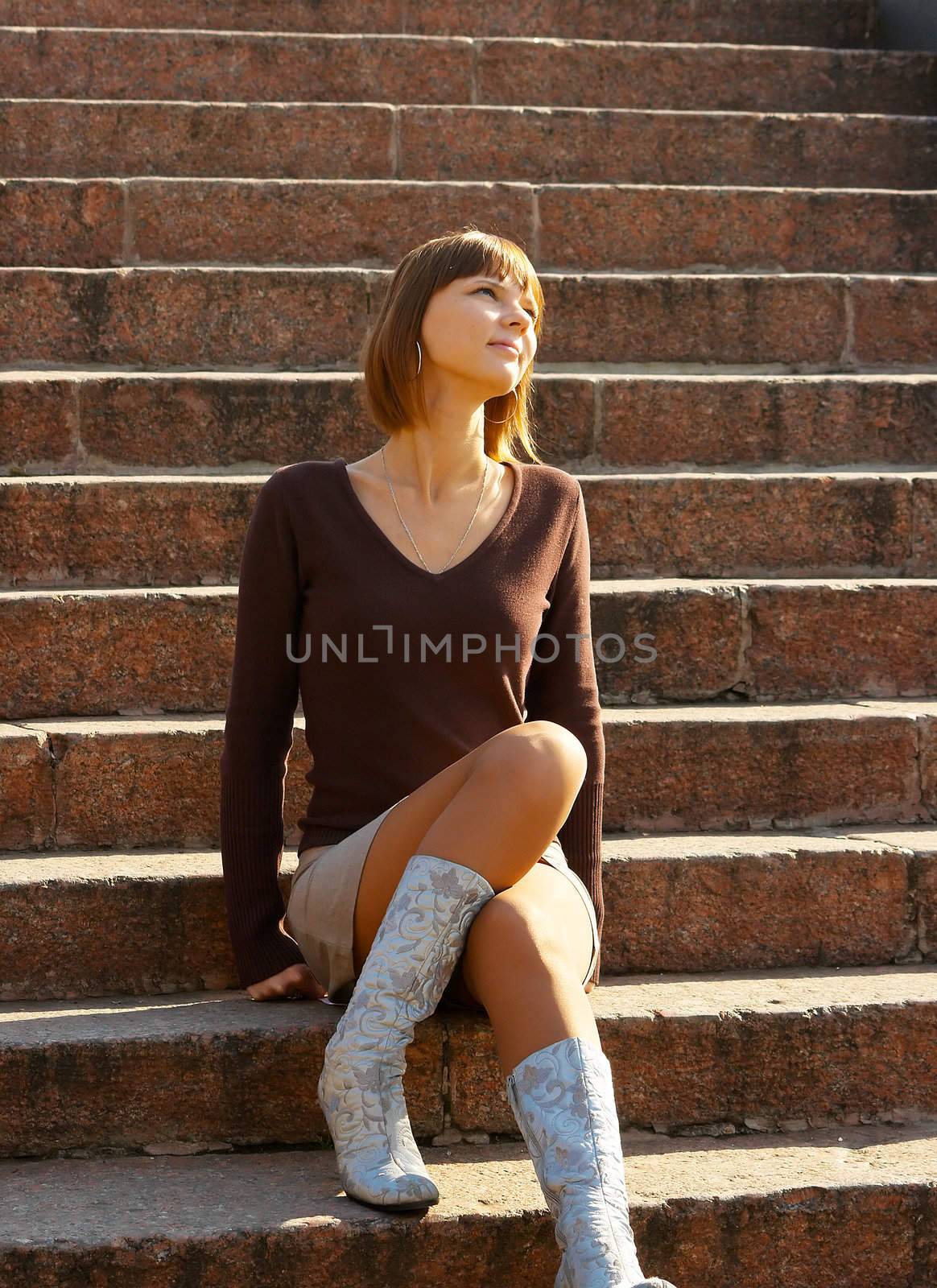 The romantic girl dreams and smiles, sitting at ladder steps. Outdoor, park