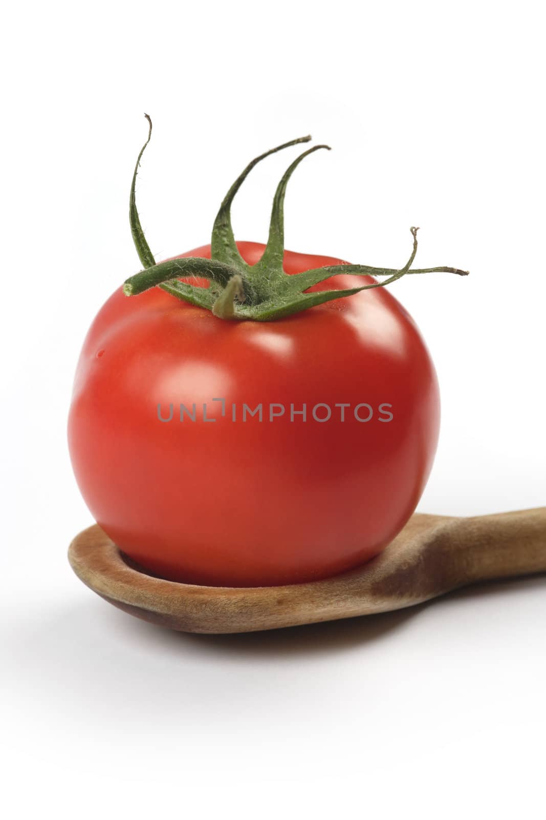 Single tomato sitting in an old wooden spoon.