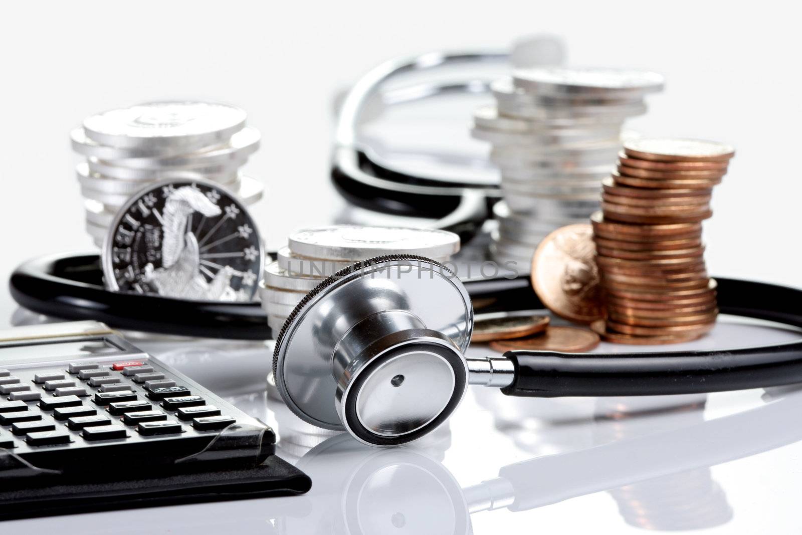 Financial health concept, stethoscope weaving around stacks of silver and gold coins and calculator