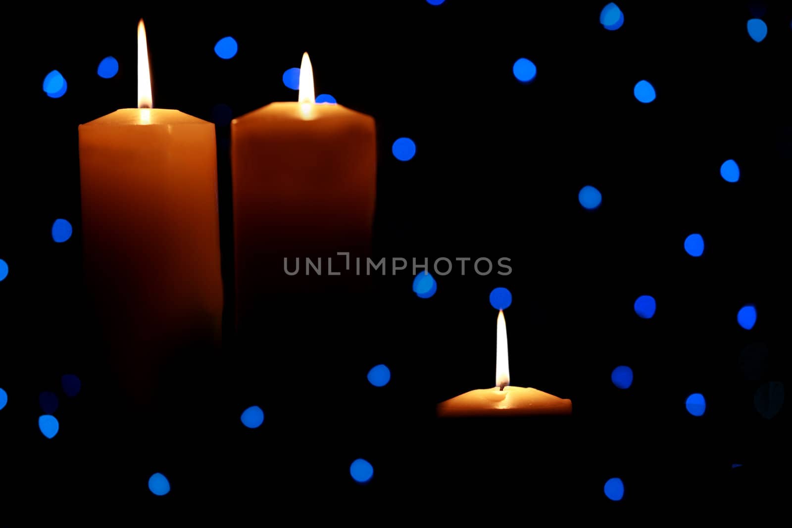 Three burning candles with blue lights in background, dark shadows