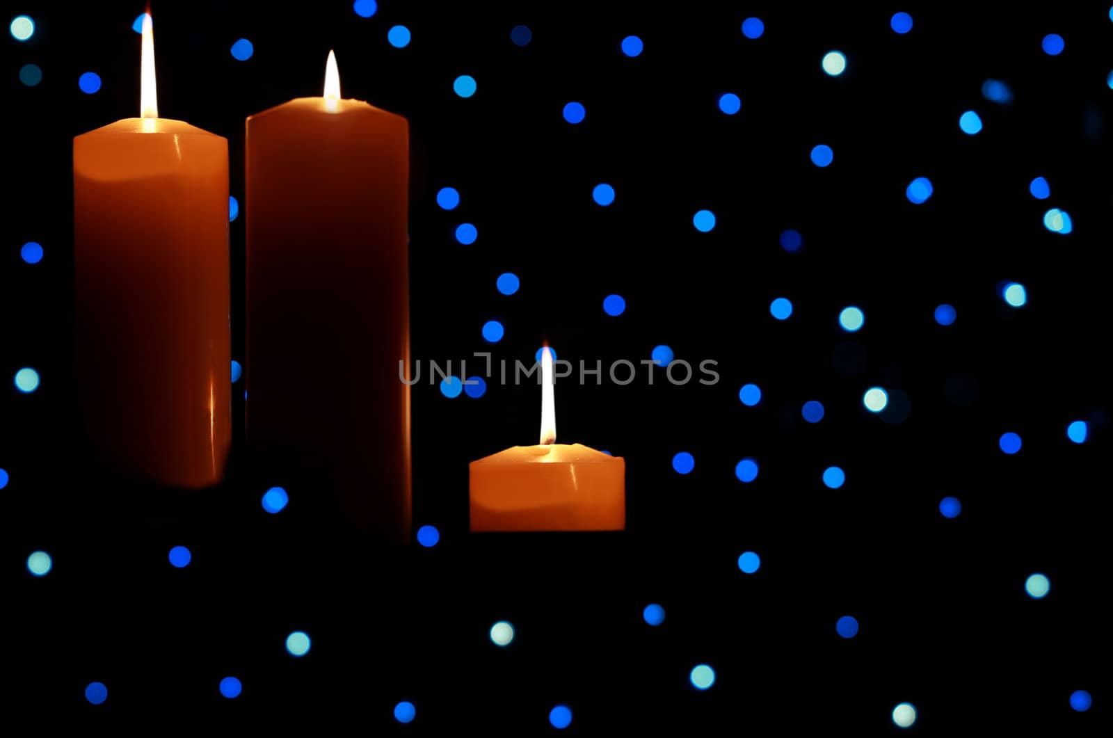 Three burning candles with blue lights in background, dark shadows