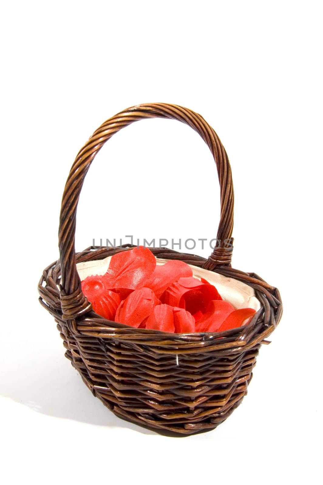 wicker basket filled with red rose peddles on a white background