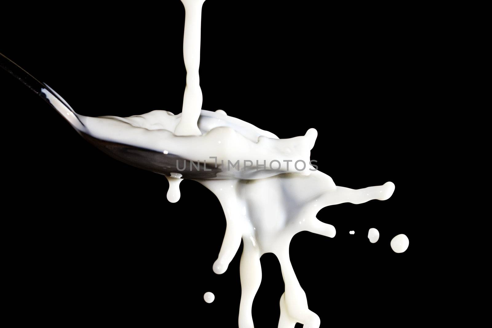 some milk flows over a spoon with black background