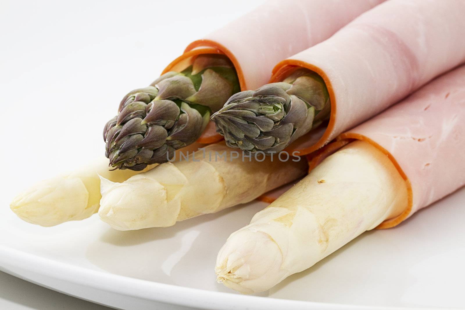 some green and white asparagus enrolled with ham on a white plate