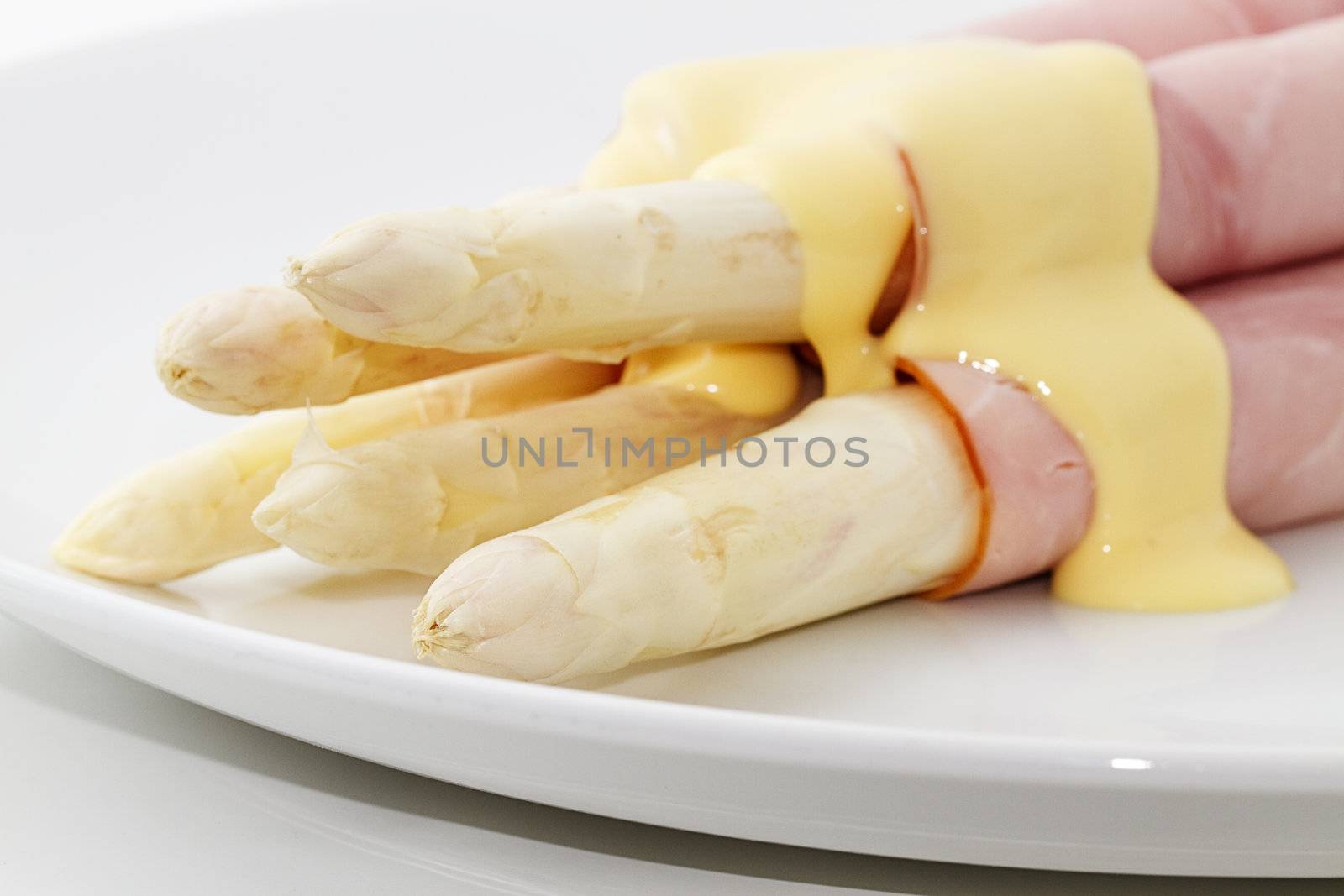 some asparagus enrolled with ham covered with dressing on a white plate
