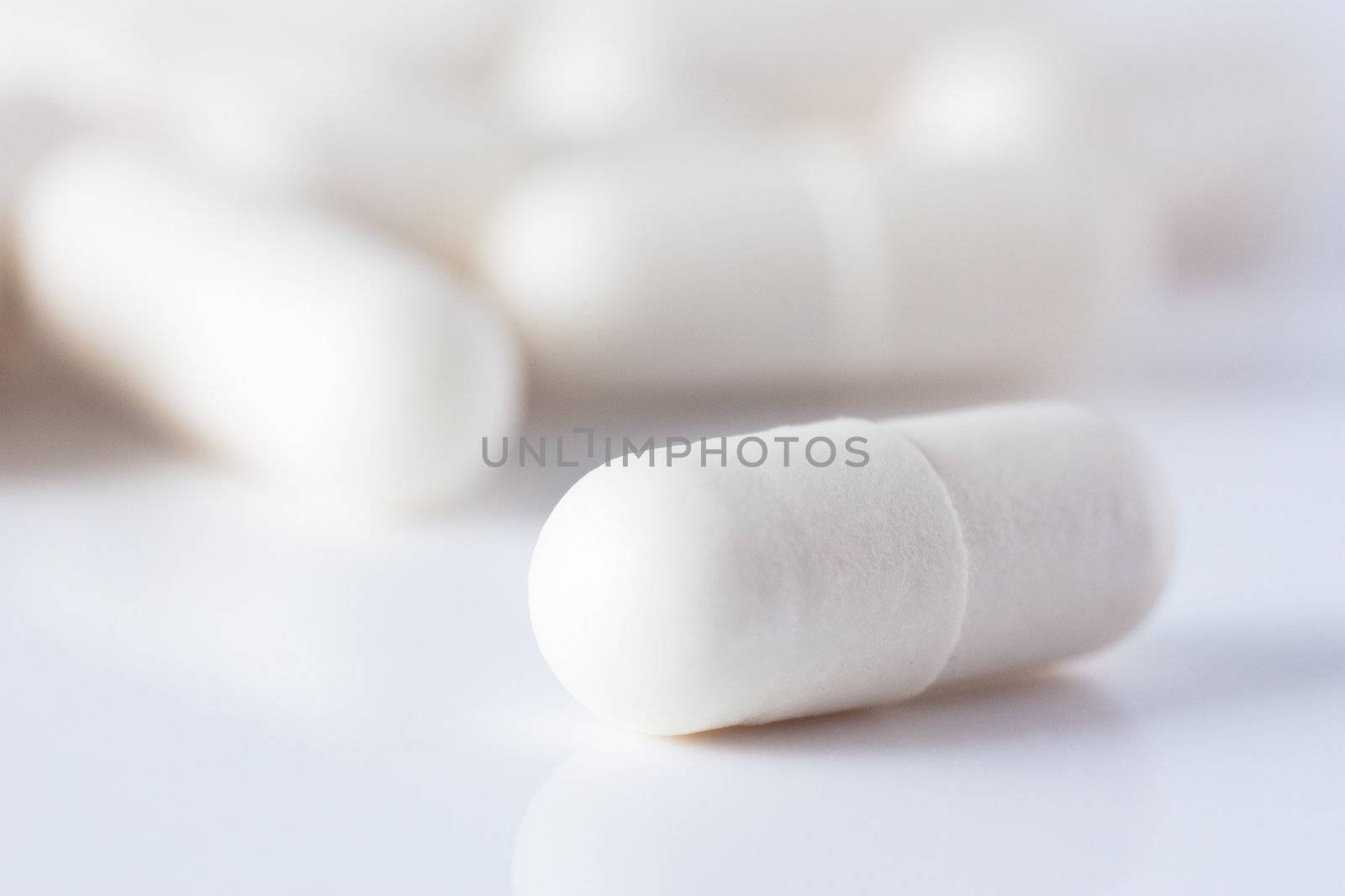 Macro shot of white capsuled pill and a heap of same pills defocused on background