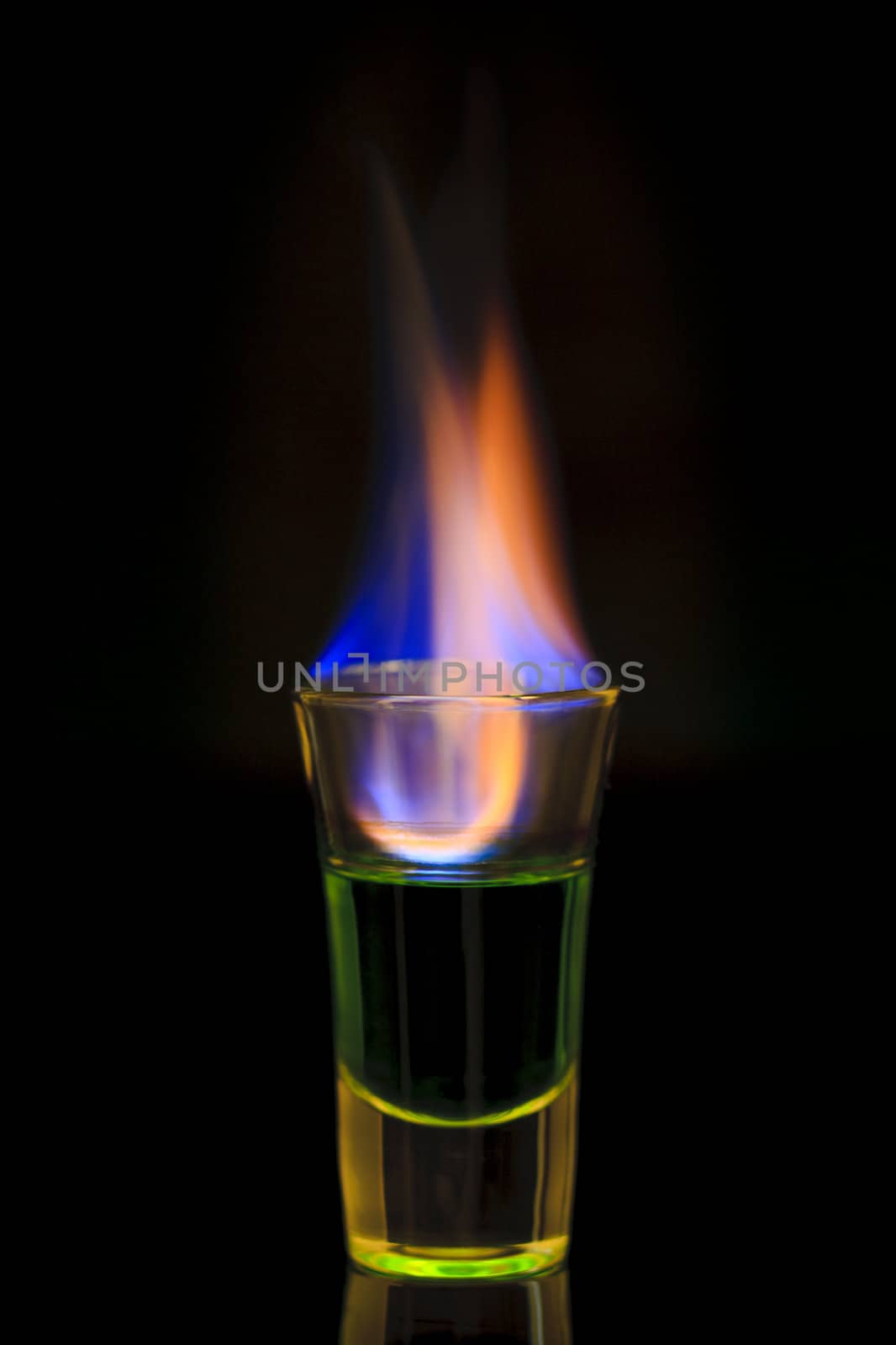 Green absinth drink on fire over black background