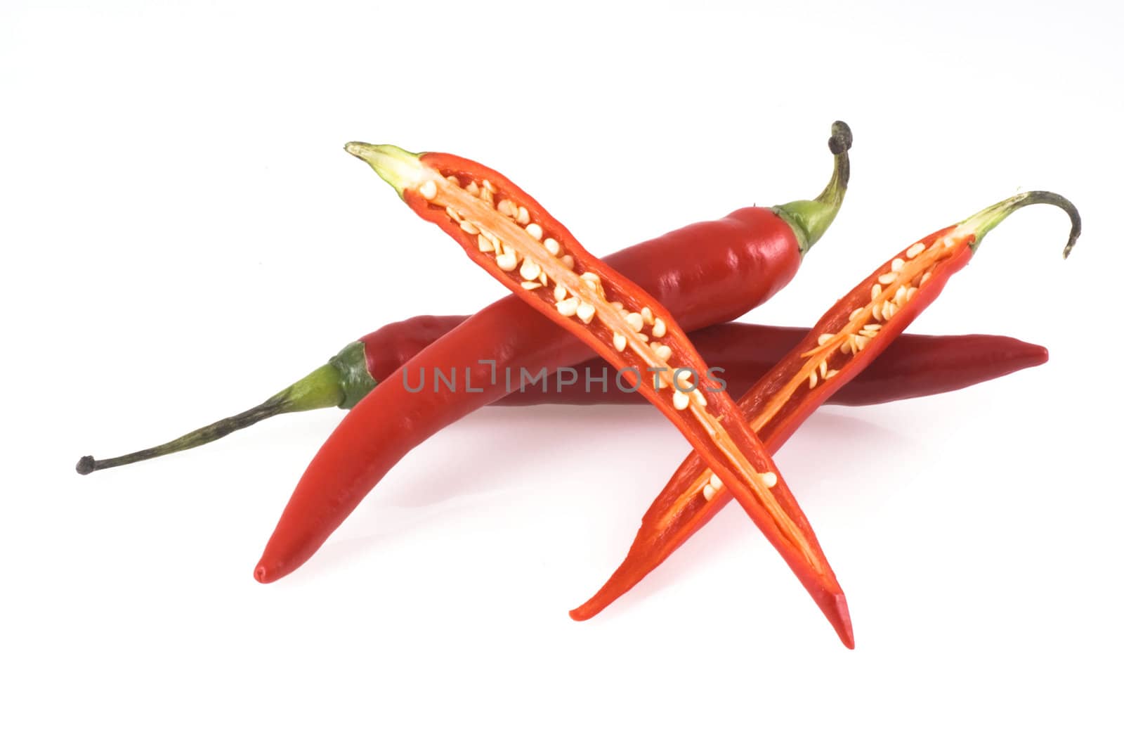 Three red chili peppers on a white background, two unimpaired and one cut open.