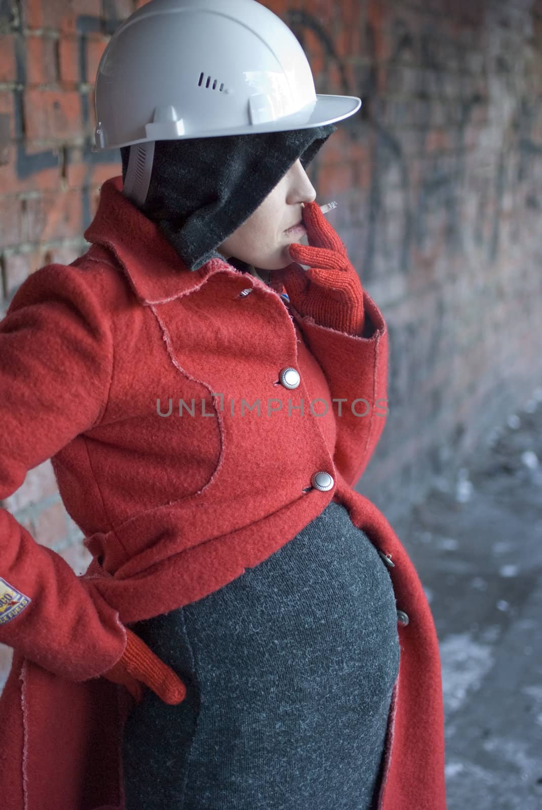 Pregnant woman in red coat and helmet smokes a cigarette