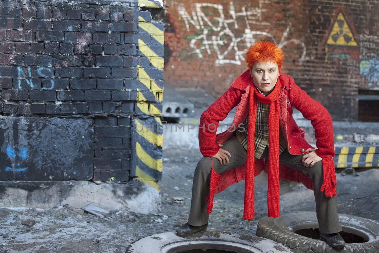 Red-haired woman stands on the old tires in active and strong pose. She is stright looking to the camera
