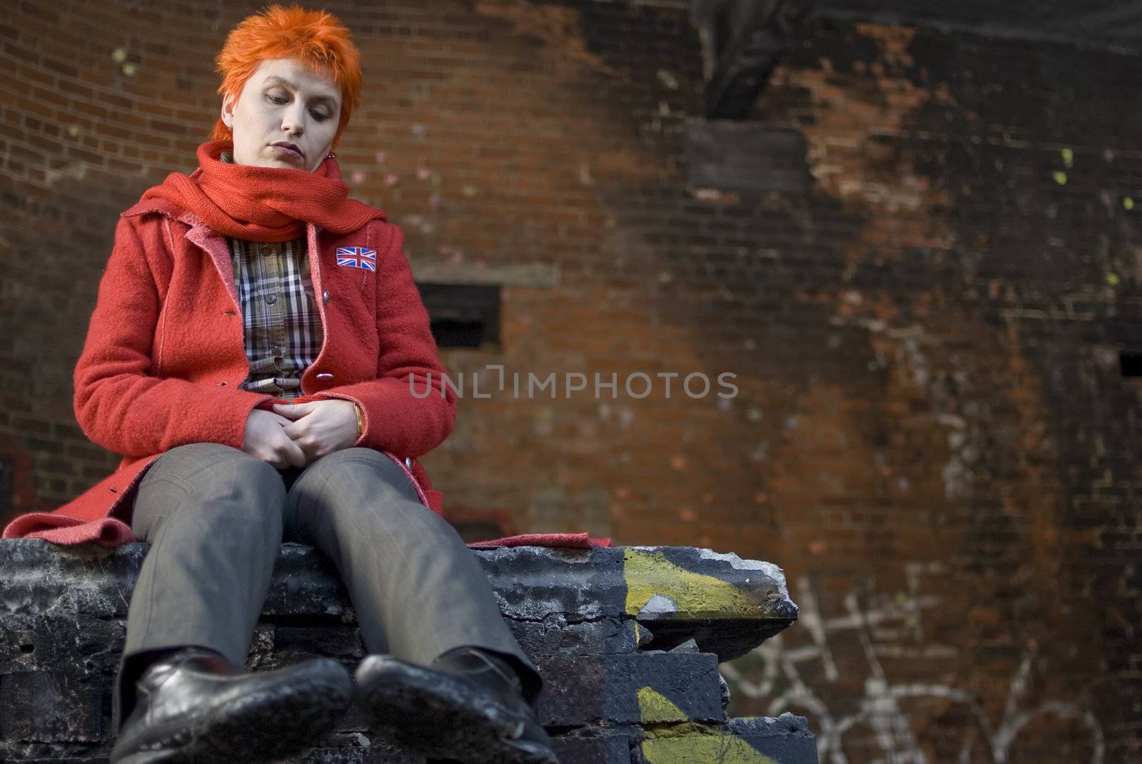Red-haired woman sits on the edge of the wall with sadness and melancholy