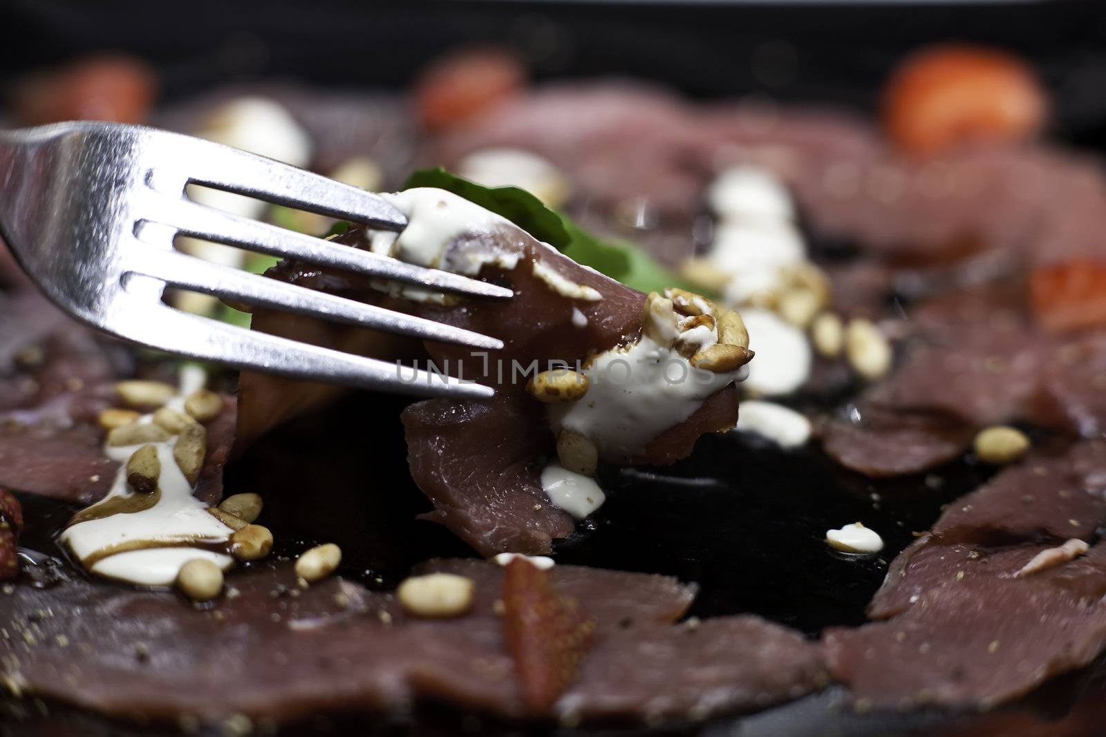 springbok carpaccio with a white sauce, strawberries and nuts on a black plate