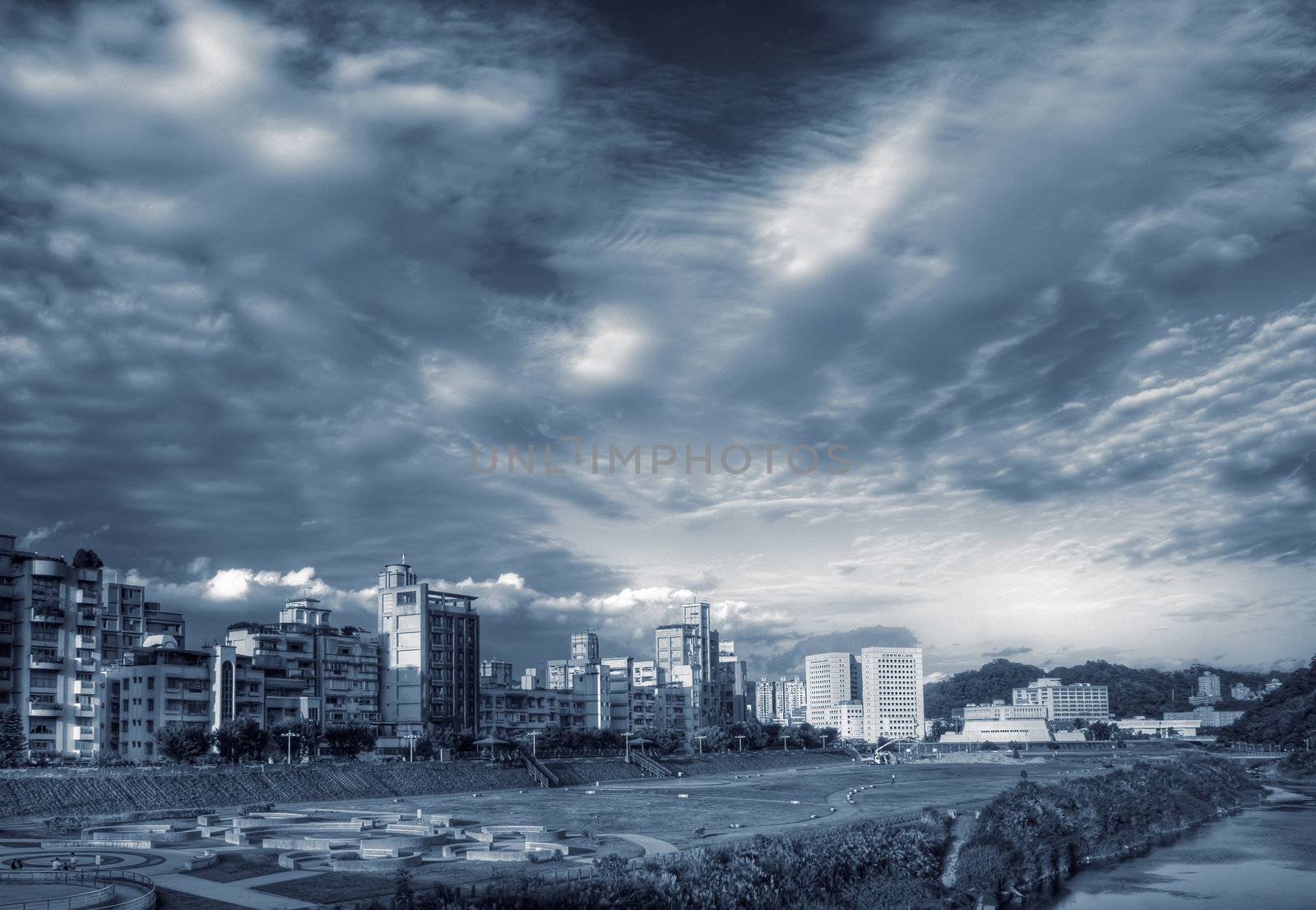 City scenery with building near park and river under dramatic sky.