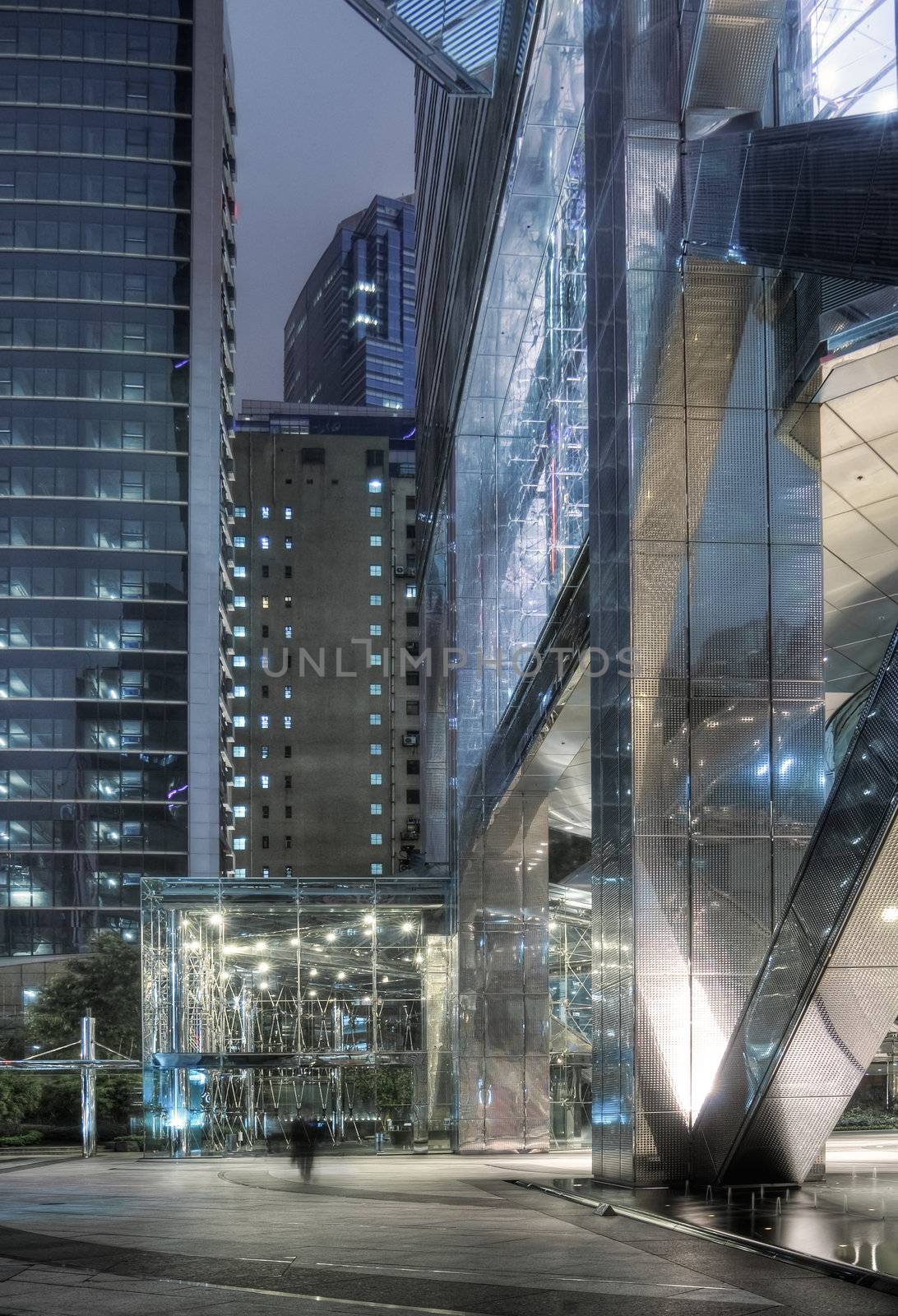 Modern skyscraper exterior with businessman walk blurred in night.