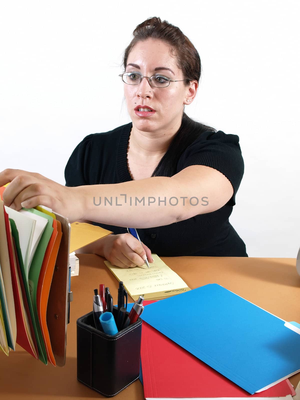 A female office worker checks a file as she writes the on a notepad.