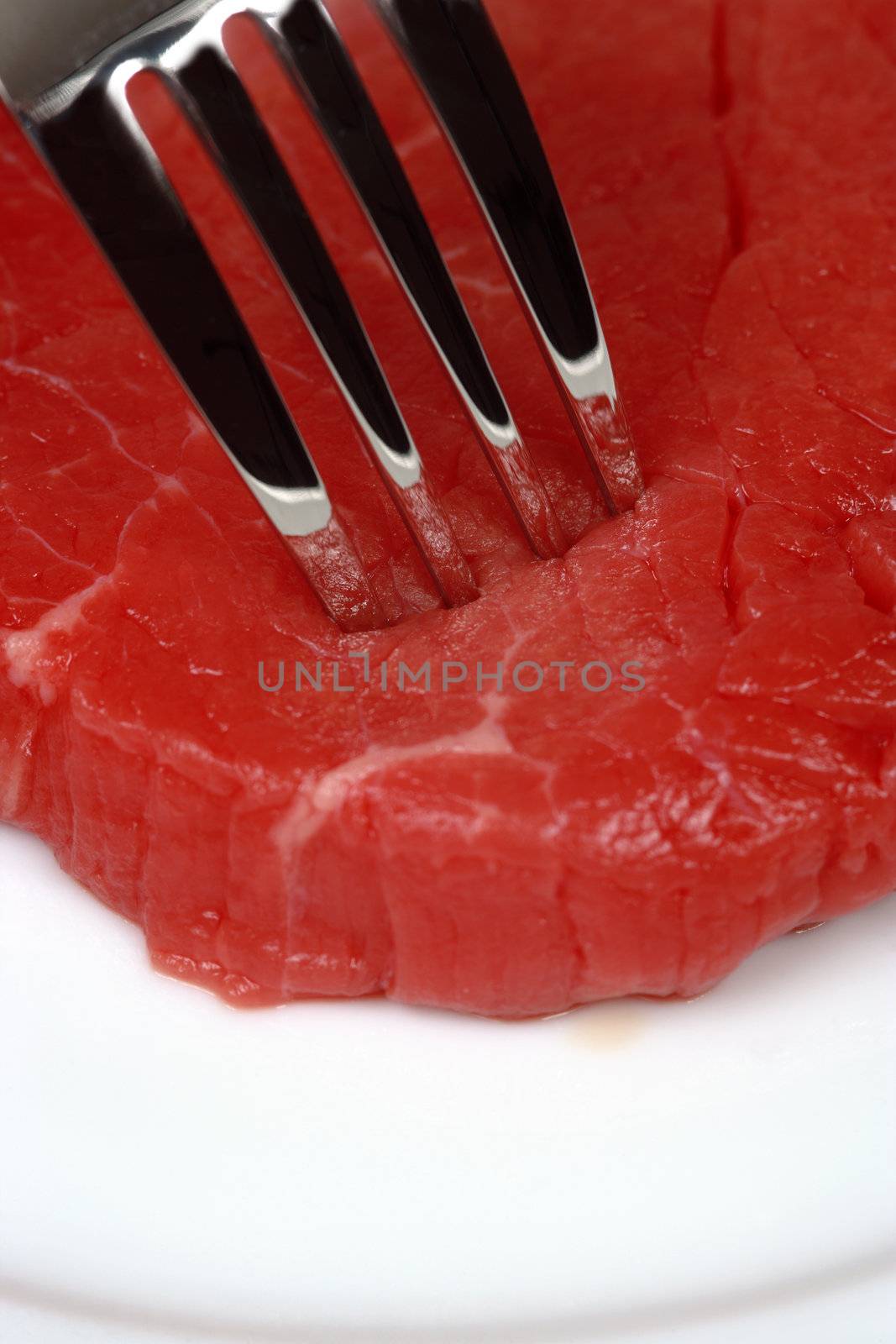 Dinner plate with a fork piercing raw red meat.

