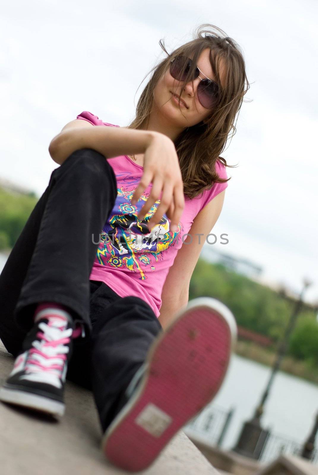 teenage girl in sunglasses and sneakers sitting on the embankment