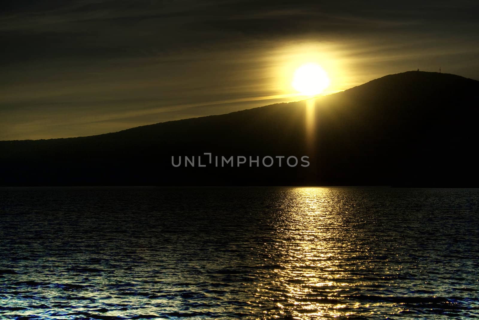 The sun setting over a lake, behind a mountain