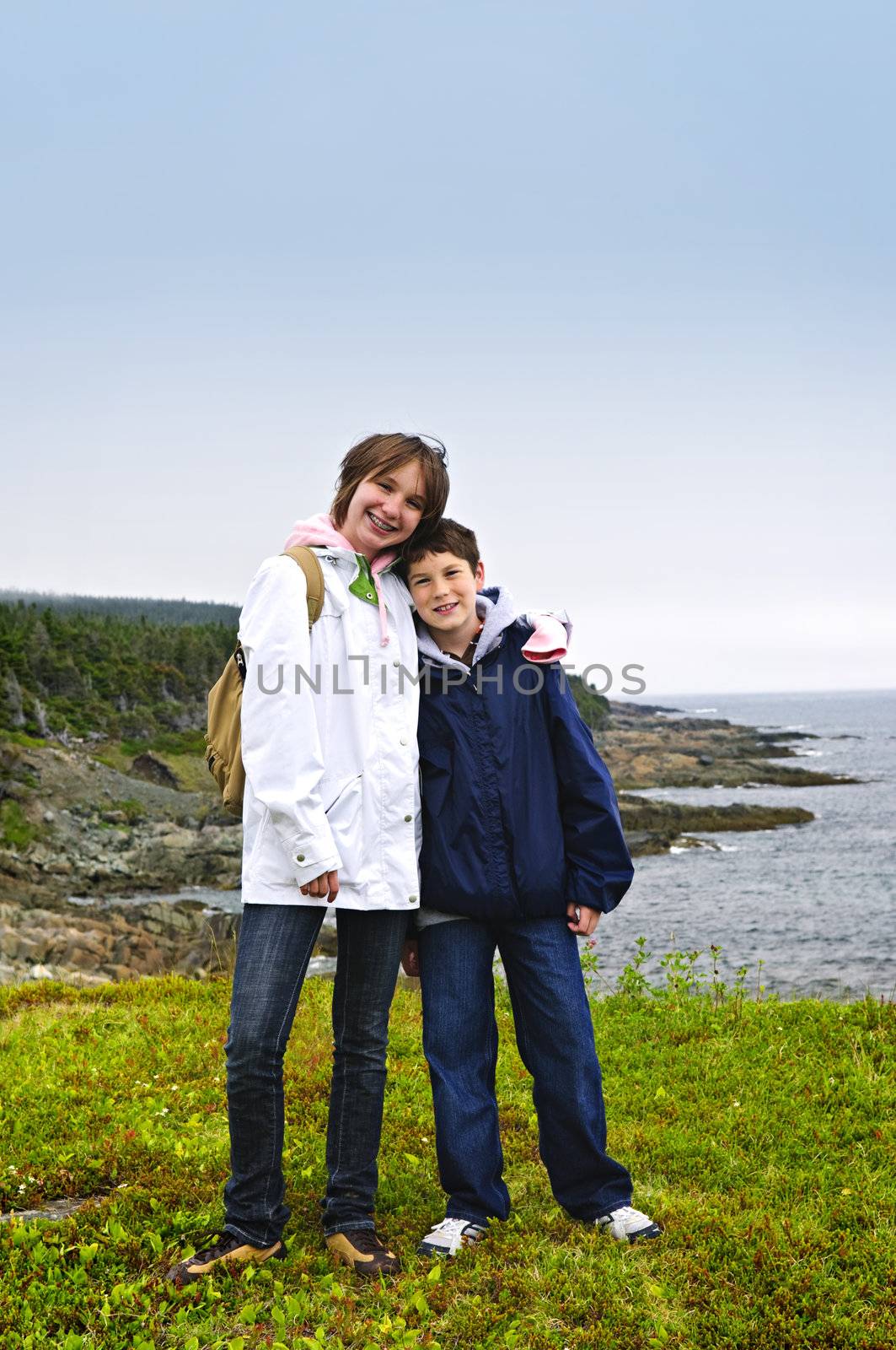 Children smiling at coastal view of rocky Atlantic shore in Newfoundland, Canada