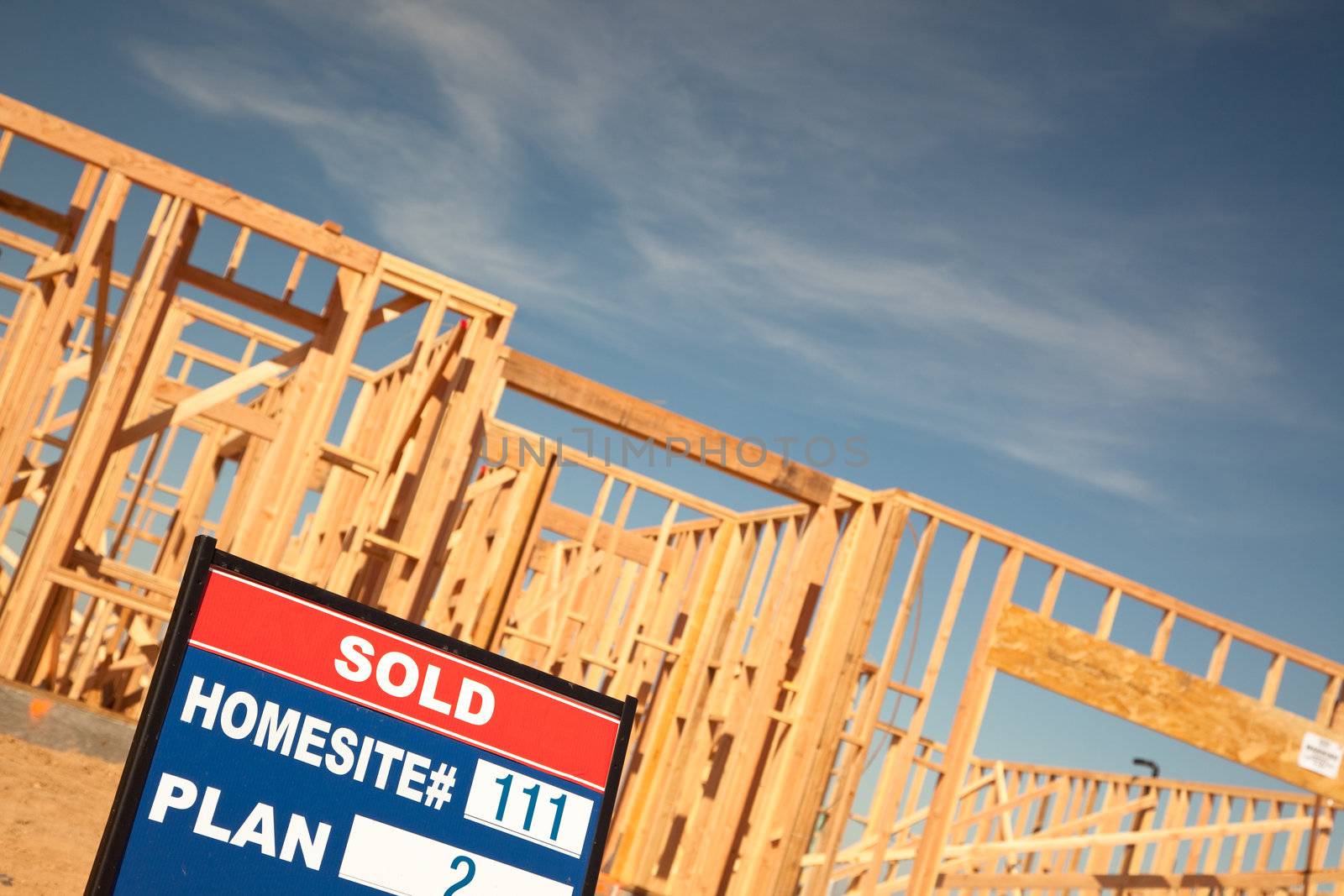 Sold Lot Real Estate Sign at New Home Framing Construction Site Against Deep Blue Sky.