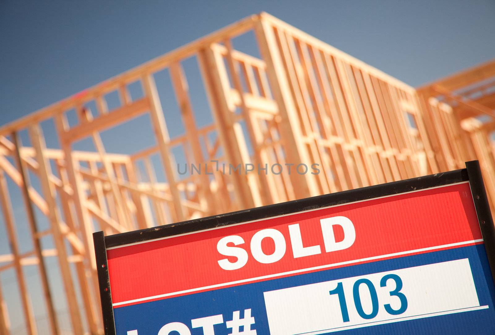 Sold Lot Real Estate Sign at New Home Framing Construction Site Against Deep Blue Sky.